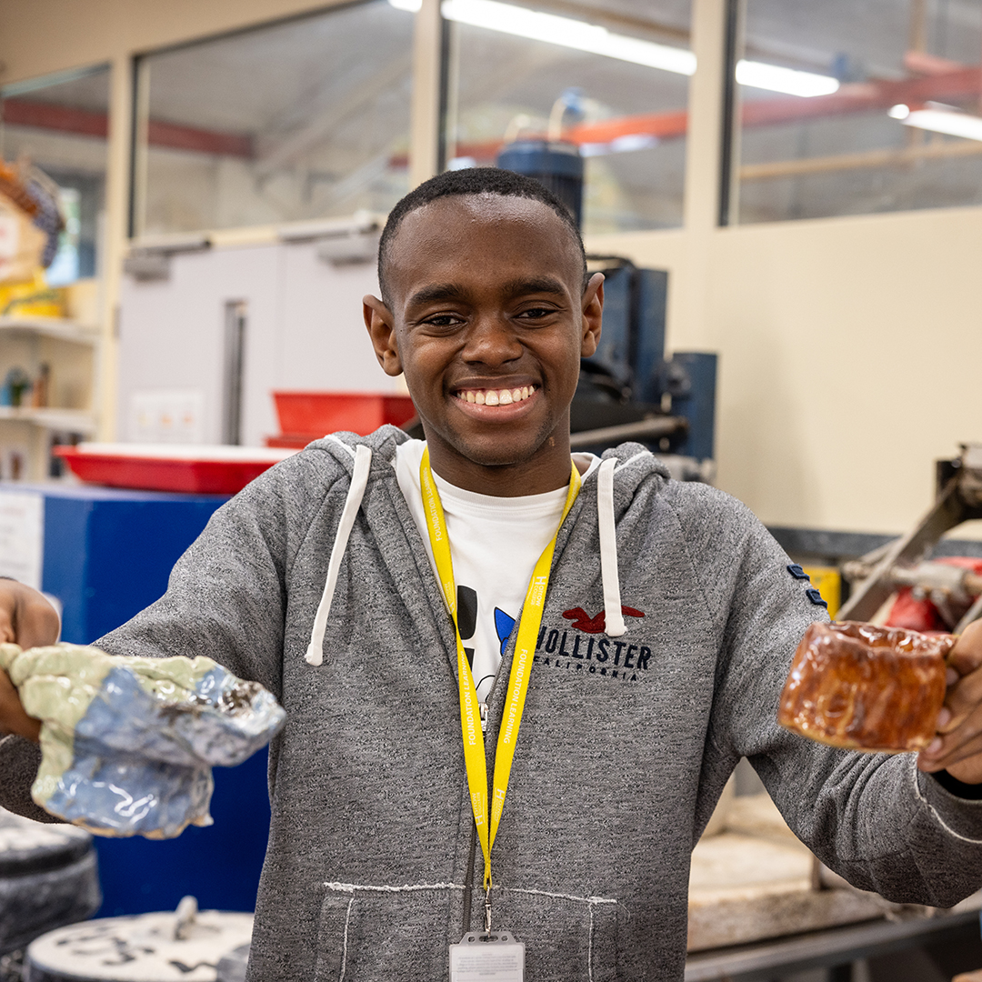 Foundation Learning Student holding 2 pieces of pottery art work and smiling at the camera