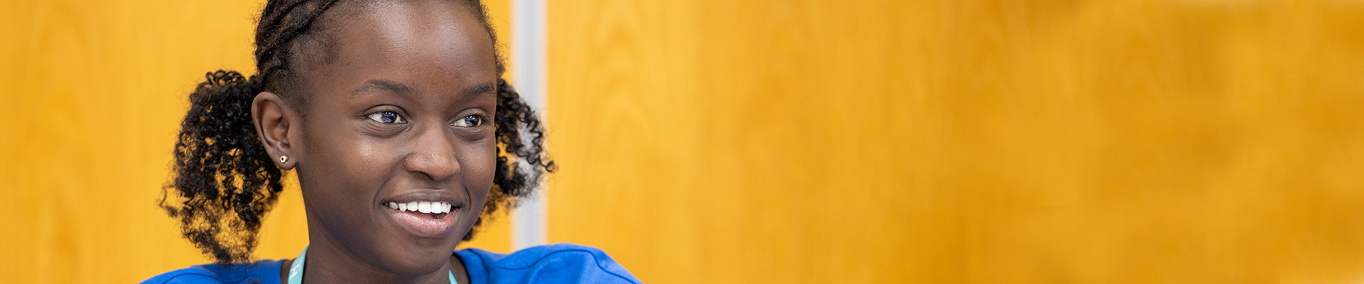 Female Harrow College student smiling into the distance. She is wearing a blue top.