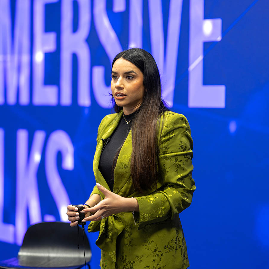 Former BBC The Apprentice winner and outstanding businesswoman Harpreet Kaur visited Harrow , Richmond, and Uxbridge Colleges (HRUC) for its first-ever Immersive Talk on 3 March 2025. Harpreet is standing in front of a blue screen, wearing a green jacket.